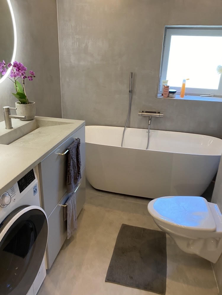 Badrum i ljusgrå microcement – tvättmaskin, badkar
